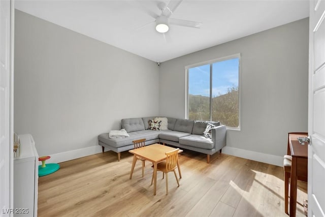 living room featuring a ceiling fan, baseboards, and light wood finished floors