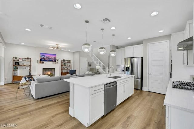 kitchen with a sink, under cabinet range hood, a lit fireplace, appliances with stainless steel finishes, and light countertops