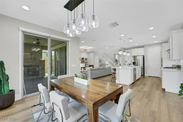 dining area with light wood finished floors, visible vents, a stone fireplace, and a ceiling fan