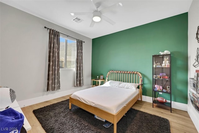 bedroom featuring visible vents, an accent wall, baseboards, and wood finished floors