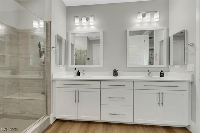 bathroom with a sink, double vanity, wood finished floors, and a shower stall