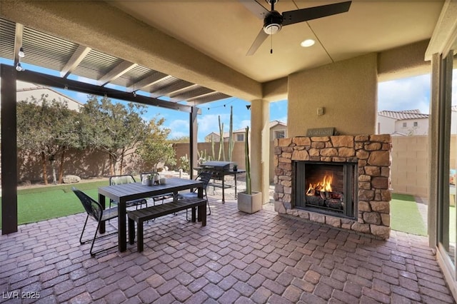 view of patio with ceiling fan, outdoor dining area, an outdoor stone fireplace, and a fenced backyard