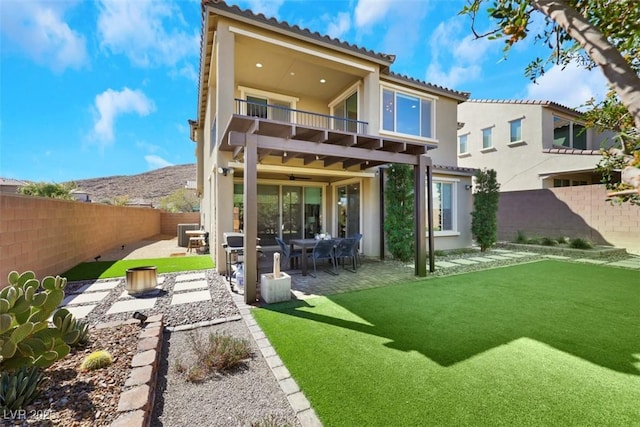 back of house with a balcony, a fenced backyard, a lawn, and a patio area