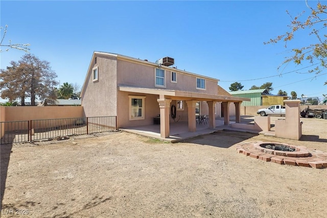 back of house featuring a fire pit, fence, stucco siding, central AC unit, and a patio area