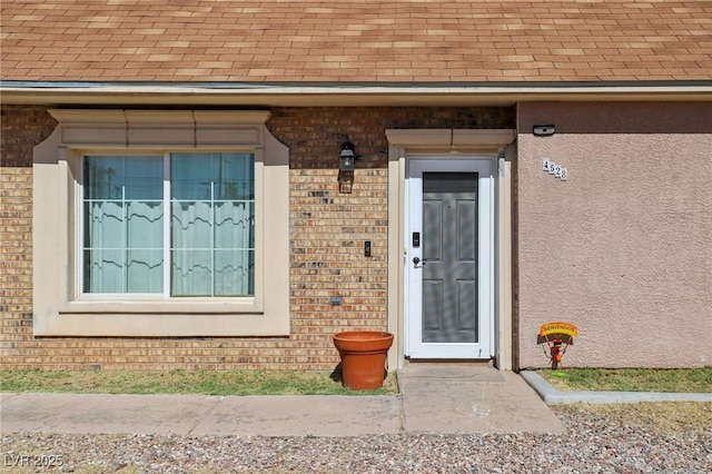 entrance to property featuring brick siding and a shingled roof