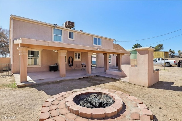 back of house with stucco siding, an outdoor fire pit, central AC unit, and a patio area