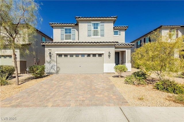 mediterranean / spanish home with decorative driveway, a tile roof, an attached garage, and stucco siding