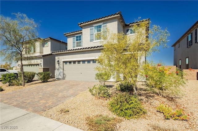 mediterranean / spanish-style house featuring stucco siding, a tile roof, decorative driveway, and a garage