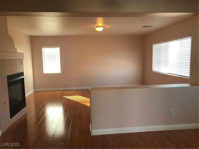 unfurnished living room with a tiled fireplace, visible vents, baseboards, and wood finished floors