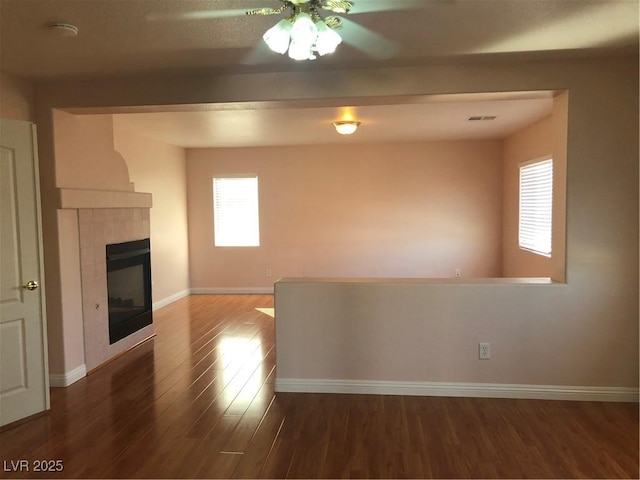 unfurnished living room with wood finished floors, visible vents, baseboards, a fireplace, and ceiling fan