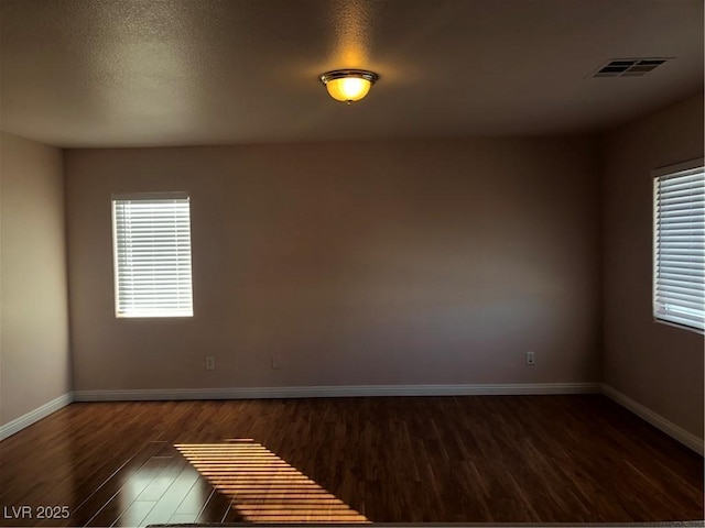 empty room with visible vents, baseboards, dark wood-style flooring, and a textured ceiling