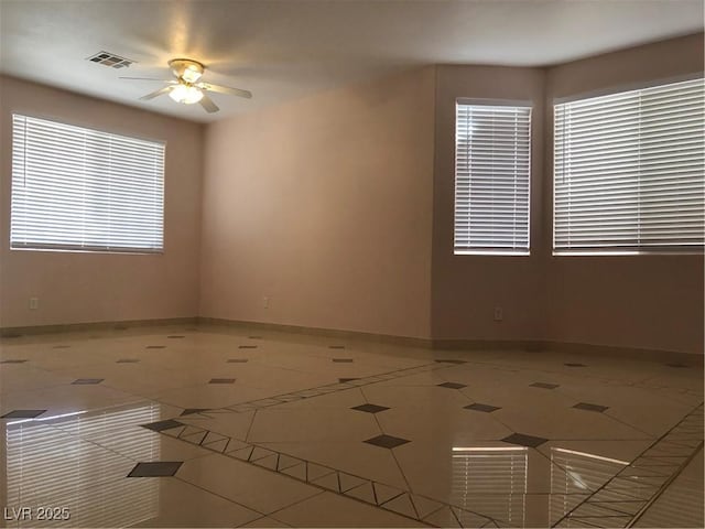 spare room with tile patterned flooring, visible vents, a ceiling fan, and baseboards