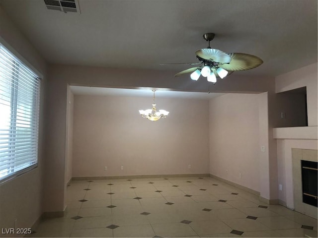 interior space featuring a tiled fireplace, visible vents, ceiling fan with notable chandelier, and baseboards