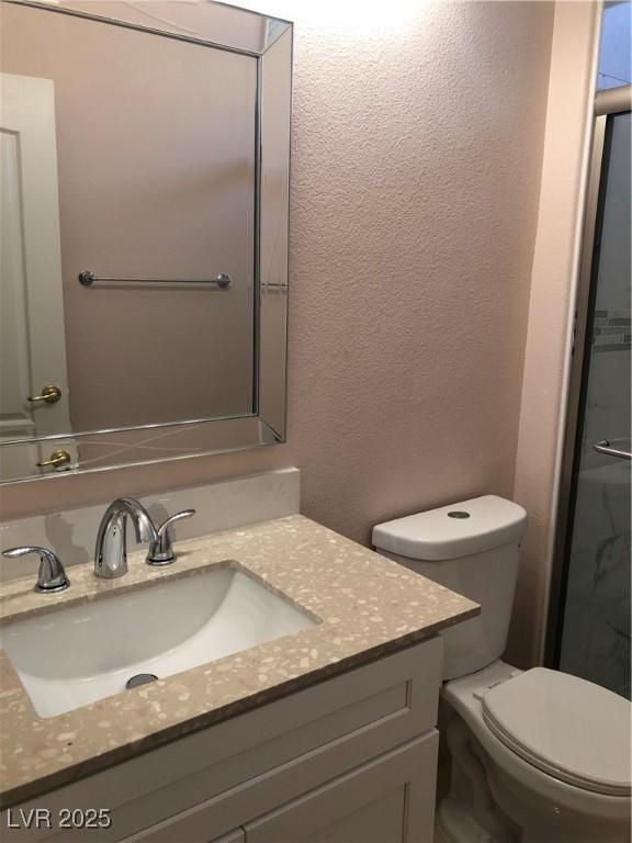 bathroom featuring toilet, vanity, and a textured wall