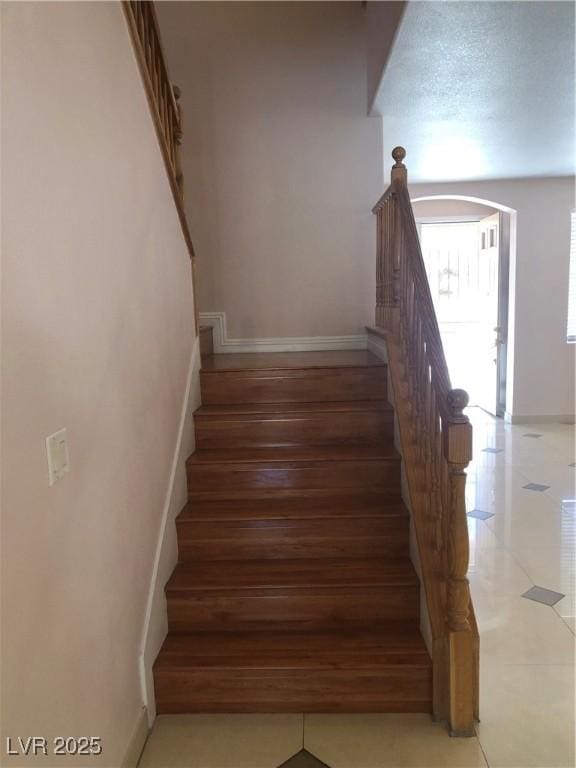 stairway featuring arched walkways and baseboards