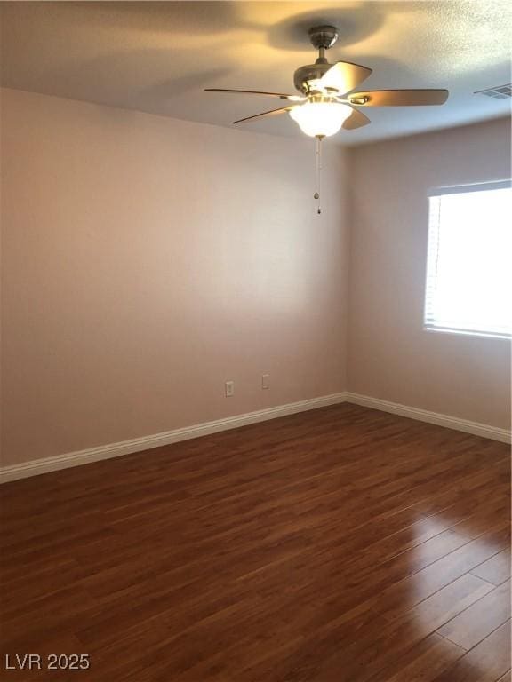 empty room with visible vents, baseboards, dark wood-type flooring, and a ceiling fan