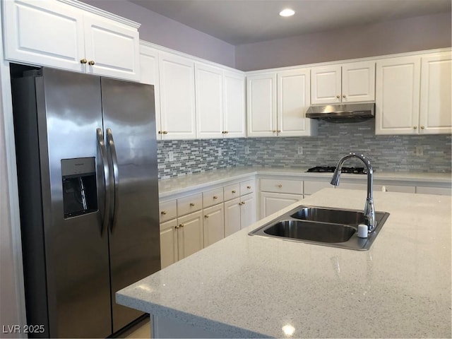 kitchen featuring a sink, decorative backsplash, white cabinets, under cabinet range hood, and stainless steel fridge