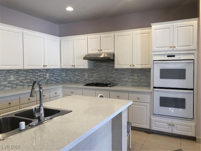 kitchen featuring under cabinet range hood, stainless steel gas cooktop, double oven, light tile patterned flooring, and a sink