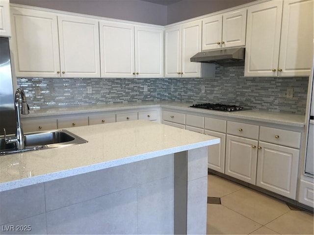 kitchen with under cabinet range hood, a sink, white cabinetry, stainless steel gas stovetop, and light tile patterned flooring