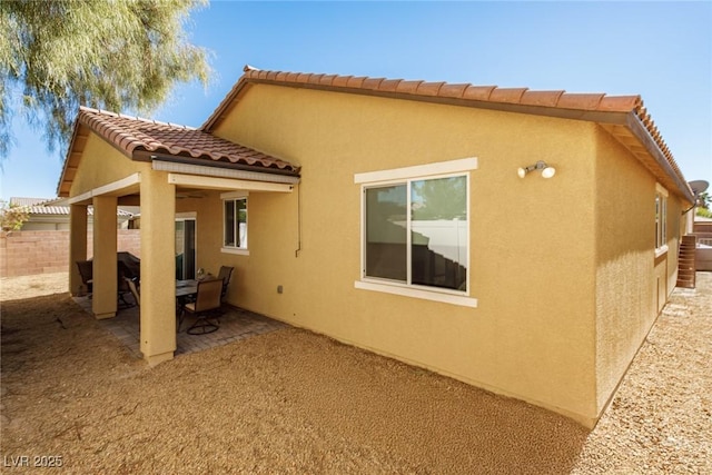 view of home's exterior with a patio area, stucco siding, a tile roof, and fence