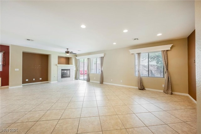 unfurnished living room with a tiled fireplace, light tile patterned floors, visible vents, and plenty of natural light