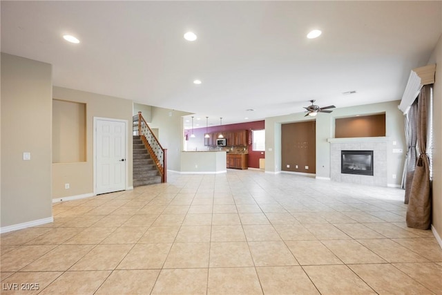 unfurnished living room featuring a tiled fireplace, recessed lighting, light tile patterned flooring, ceiling fan, and stairs