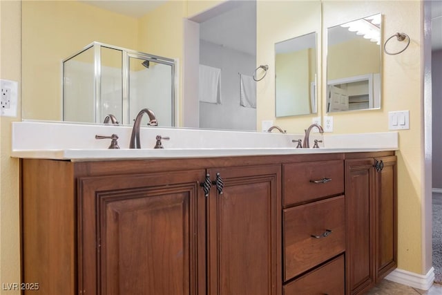 full bath with a shower stall, double vanity, baseboards, and a sink