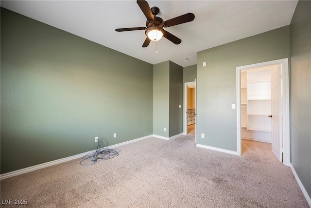 unfurnished bedroom with light carpet, a ceiling fan, a walk in closet, and baseboards