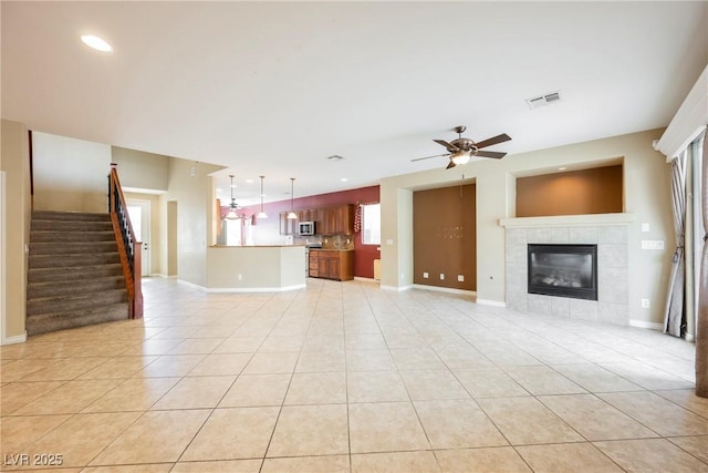 unfurnished living room featuring light tile patterned floors, stairway, baseboards, and a tile fireplace