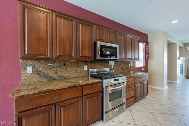 kitchen with stone countertops, appliances with stainless steel finishes, light tile patterned floors, decorative backsplash, and baseboards