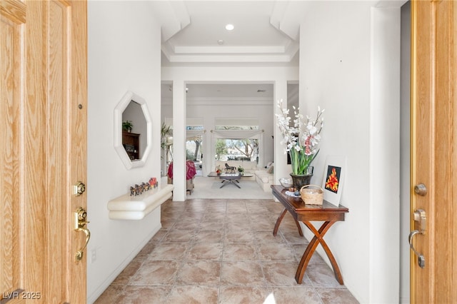 entryway featuring a high ceiling, a raised ceiling, and baseboards