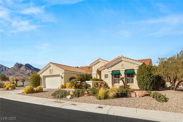 mediterranean / spanish-style house with stucco siding, driveway, a tile roof, a mountain view, and a garage