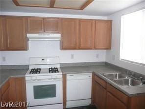 kitchen with white appliances, brown cabinets, under cabinet range hood, and a sink