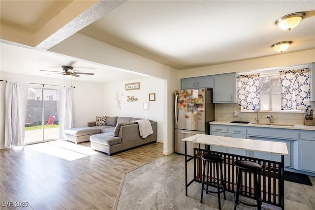 kitchen featuring freestanding refrigerator, gray cabinetry, decorative backsplash, light countertops, and a sink