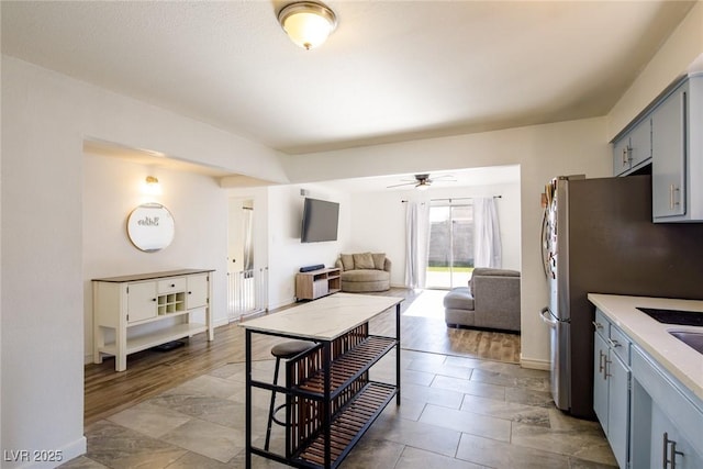 kitchen with a ceiling fan, freestanding refrigerator, gray cabinetry, light countertops, and open floor plan