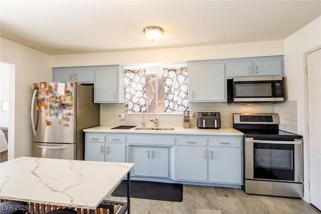 kitchen featuring gray cabinetry, a sink, stainless steel appliances, light countertops, and decorative backsplash