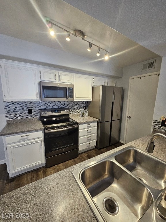 kitchen featuring dark wood-style flooring, a sink, decorative backsplash, appliances with stainless steel finishes, and white cabinetry