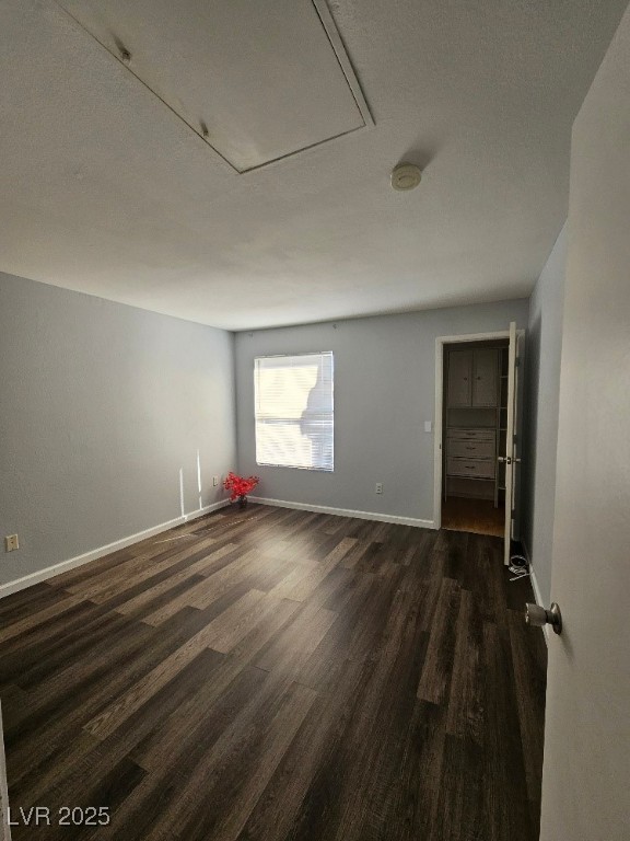 unfurnished room with attic access, baseboards, and dark wood-style flooring