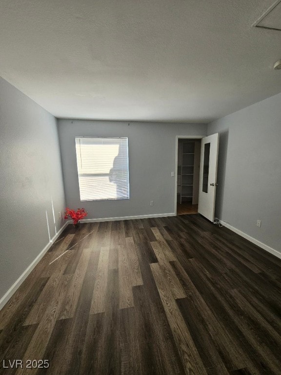 unfurnished room with baseboards, dark wood-style flooring, and a textured ceiling