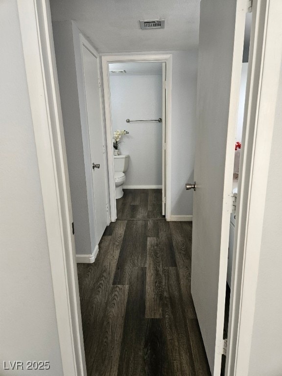 corridor featuring visible vents, baseboards, and dark wood-type flooring