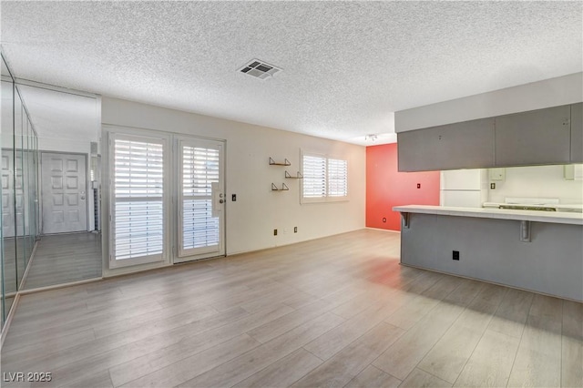 kitchen with light wood-type flooring, visible vents, a breakfast bar, a textured ceiling, and freestanding refrigerator