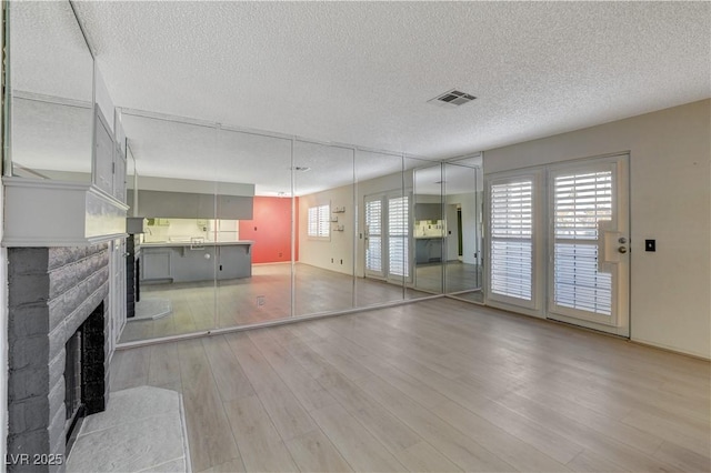 unfurnished living room featuring a fireplace with flush hearth, a healthy amount of sunlight, visible vents, and light wood finished floors