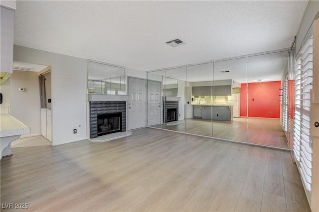 unfurnished living room featuring wood finished floors, a fireplace with raised hearth, visible vents, and a textured ceiling