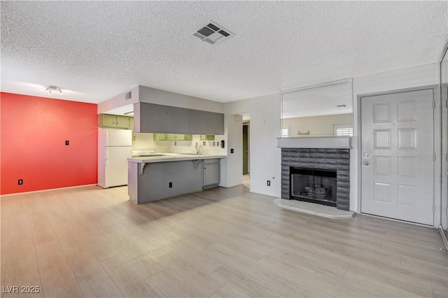 unfurnished living room with visible vents, light wood-style flooring, a tile fireplace, and a sink