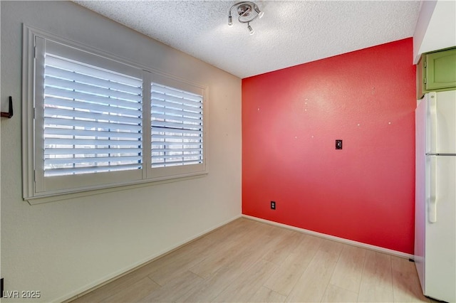 unfurnished room with a textured ceiling, baseboards, and wood finished floors