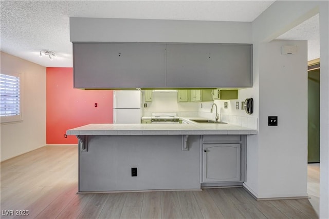 kitchen featuring a breakfast bar, a sink, electric range oven, freestanding refrigerator, and a peninsula