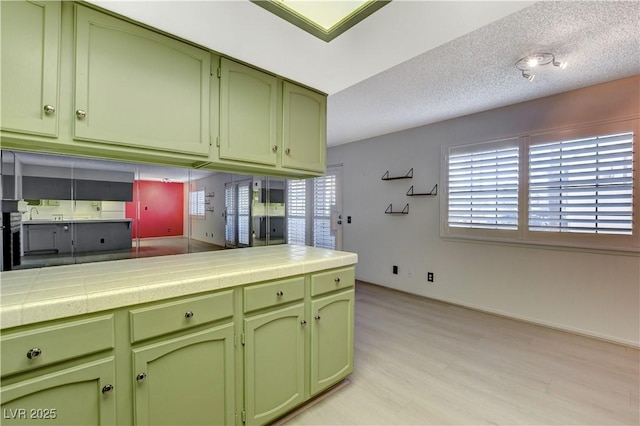 kitchen featuring tile counters, a textured ceiling, green cabinets, and light wood finished floors