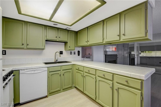 kitchen featuring a sink, white appliances, a peninsula, and green cabinetry