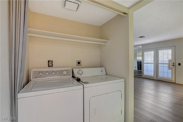 laundry area with wood finished floors, visible vents, laundry area, a textured ceiling, and washer and clothes dryer