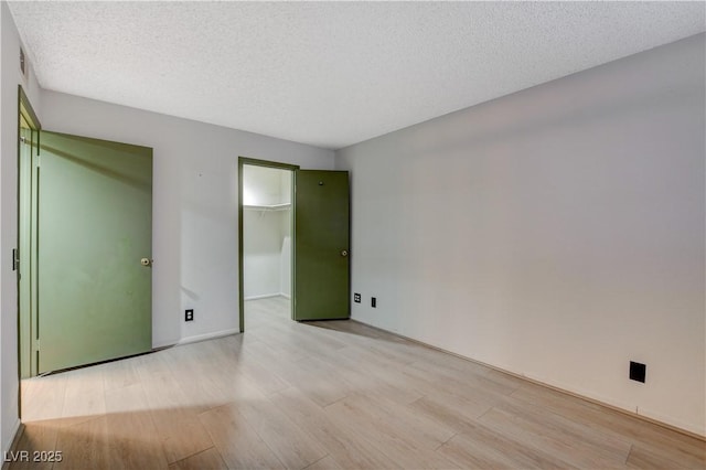 unfurnished bedroom with a spacious closet, light wood-style floors, a closet, and a textured ceiling